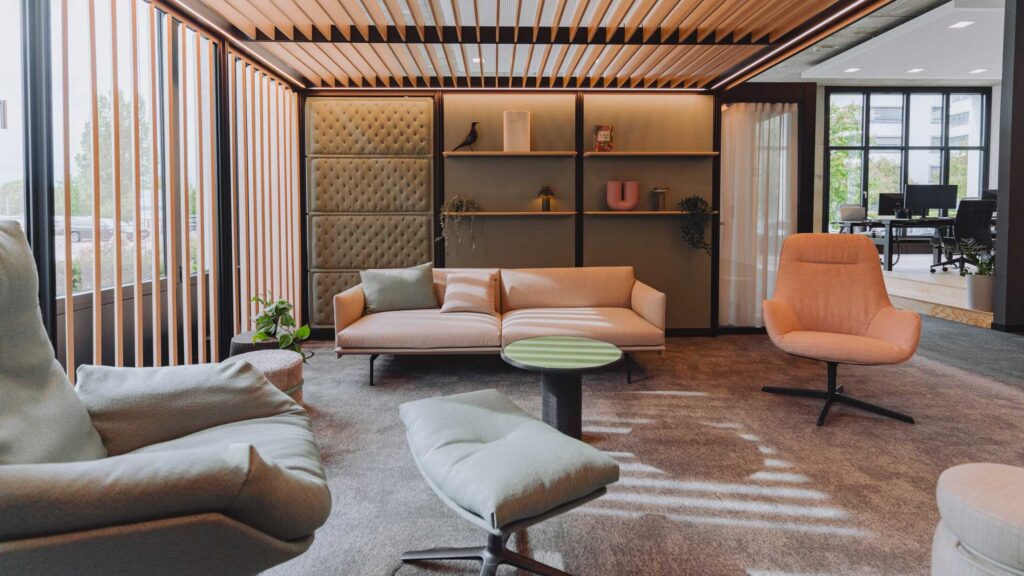 Moderne Büro-Lounge mit Holzlamellen-Decke, komfortablen Polstermöbeln und integrierten Akustikpaneelen.